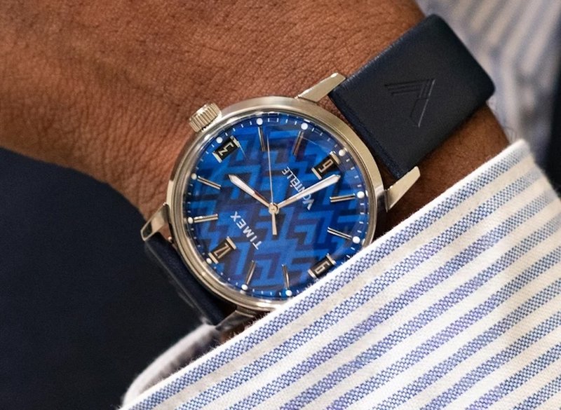 Blue patterned dial Timex Marlin watch worn on a wrist near striped shirt cuff